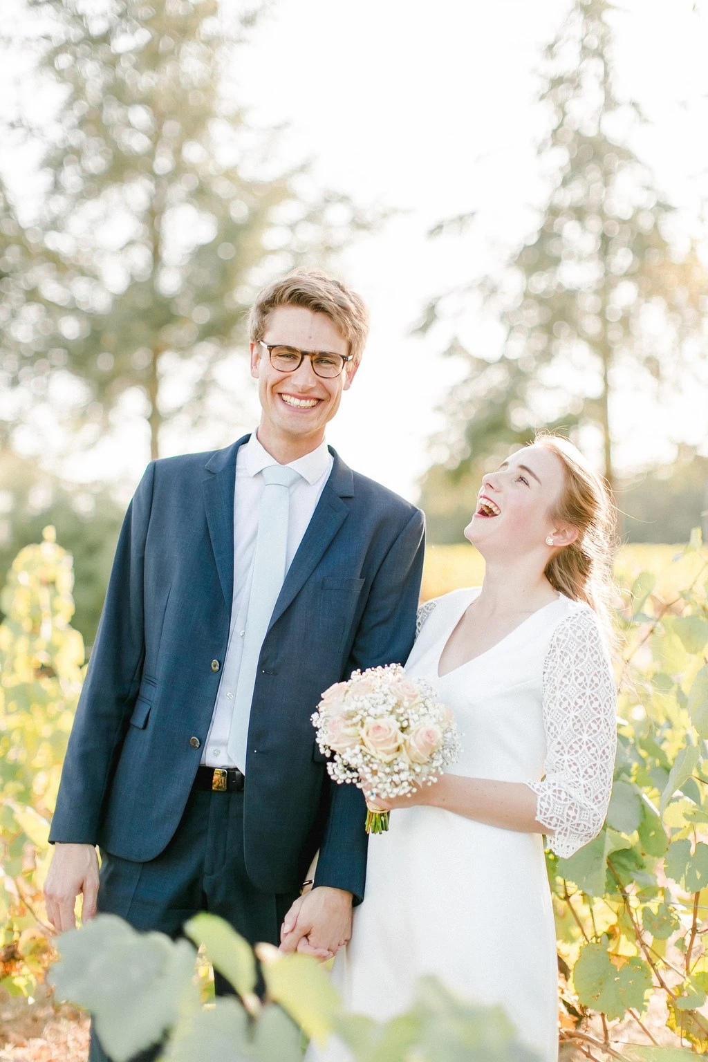 Couple de mariés riant aux éclats dans un vignoble ensoleillé, atmosphère champêtre et joyeuse