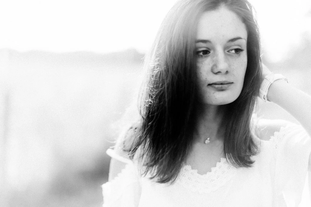 Portrait intemporel d'une jeune femme en robe blanche, regard mélancolique, lumière douce en extérieur