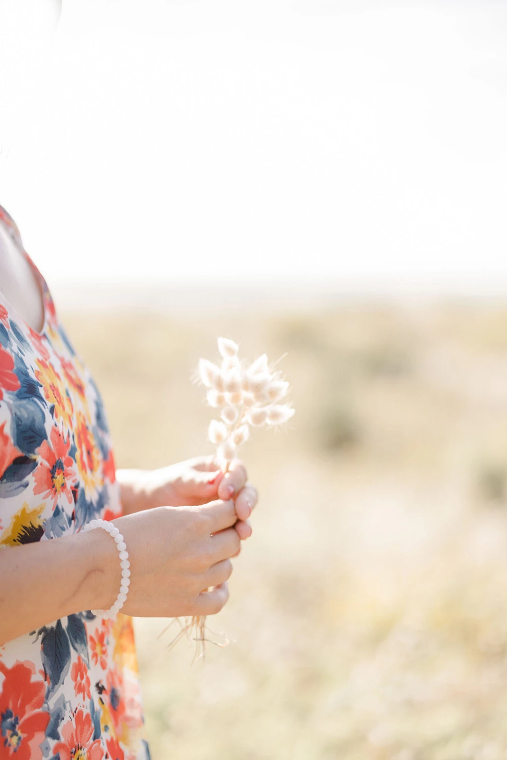 Petite fille tenant délicatement une fleur blanche séchée dans ses mains ornées d'un bracelet de perles