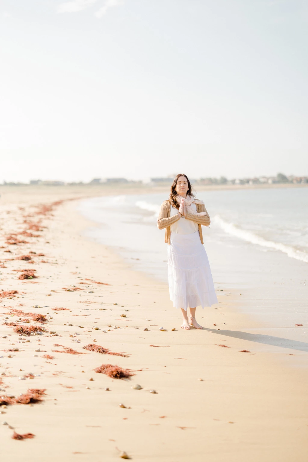 Femme en robe blanche marchant pieds nus sur une plage déserte au bord de l'océan