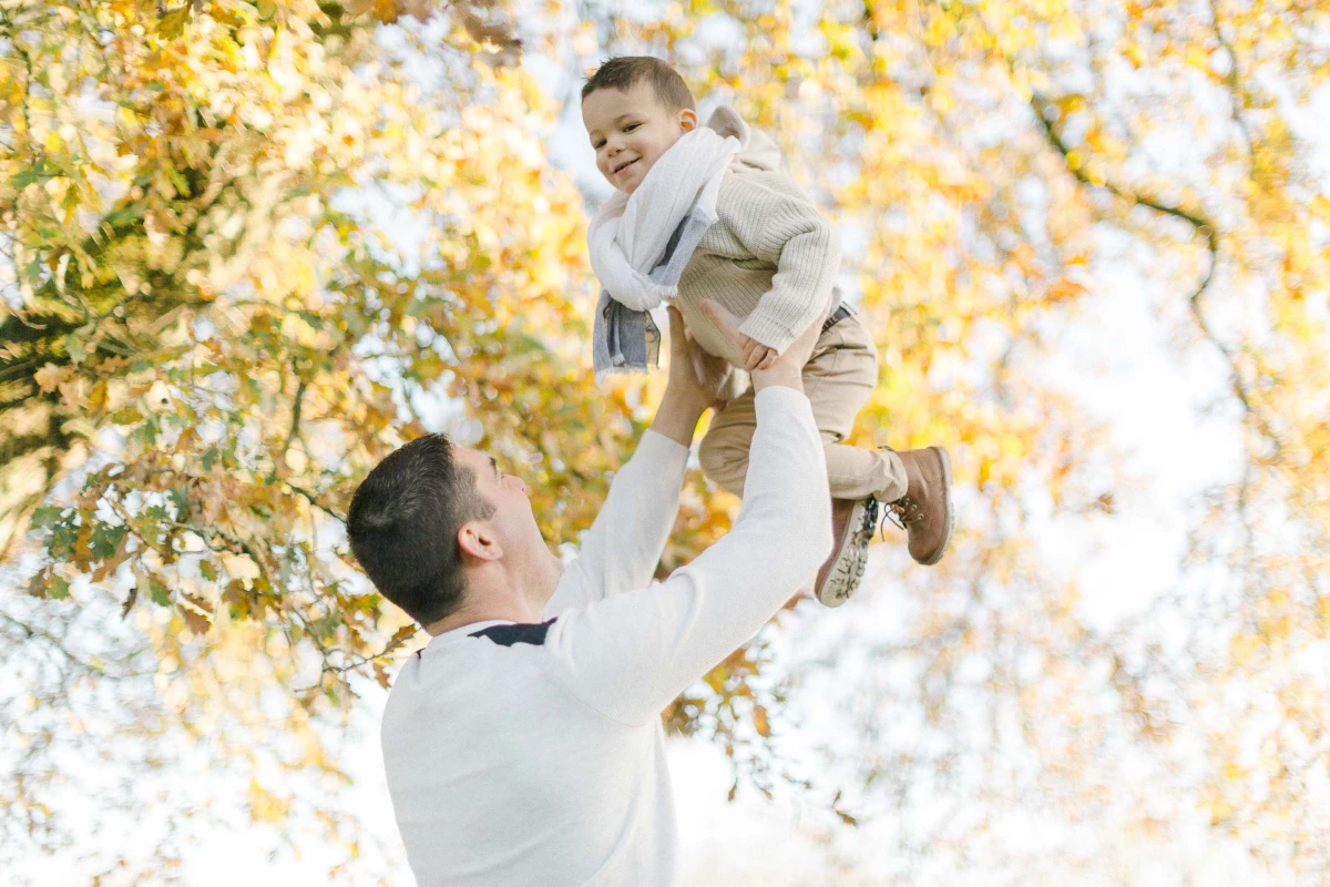 Père soulevant son enfant dans les airs lors d'une séance photo famille en automne