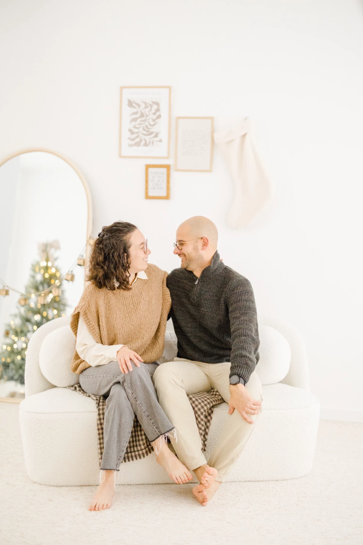 Couple complice assis sur un canapé blanc dans un décor cosy de Noël aux tons beige et naturels