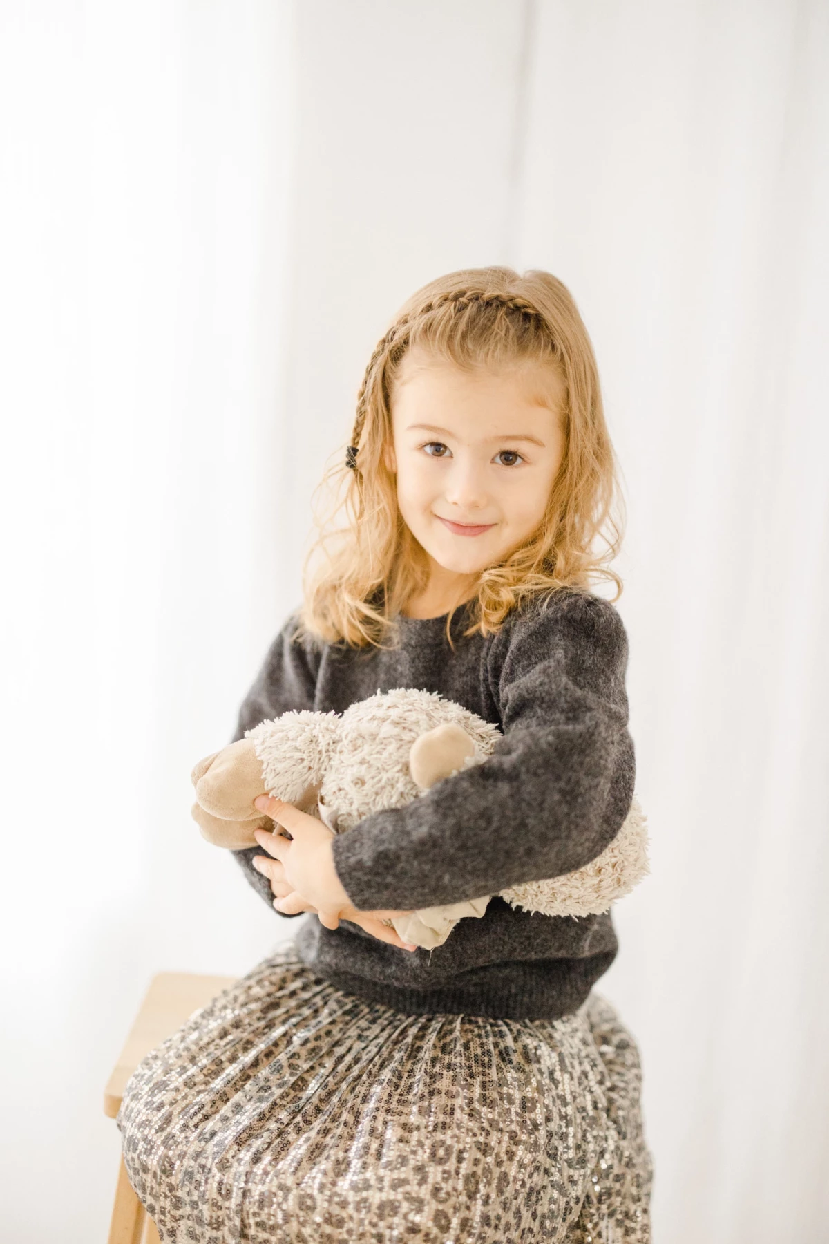 Petite fille blonde tenant tendrement sa peluche contre elle dans un studio lumineux