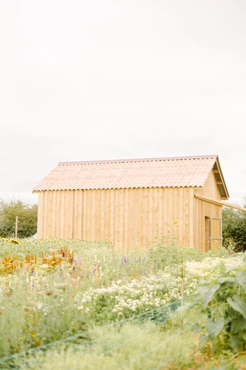 Grange en bois naturel entourée de fleurs sauvages pour une cérémonie de mariage champêtre estivale