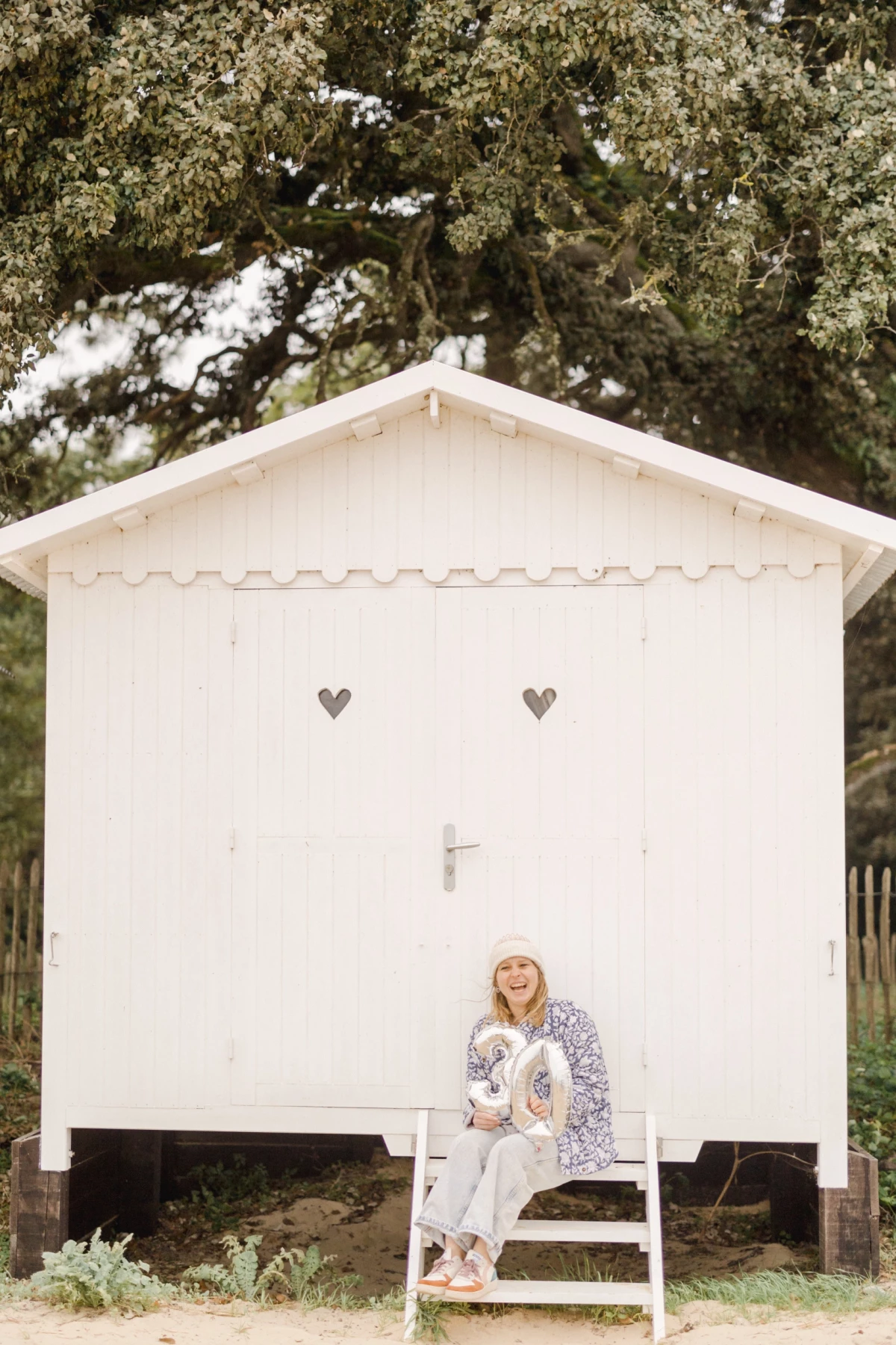 Petite fille en robe blanche assise sur les marches d'une cabane de plage décorée de cœurs