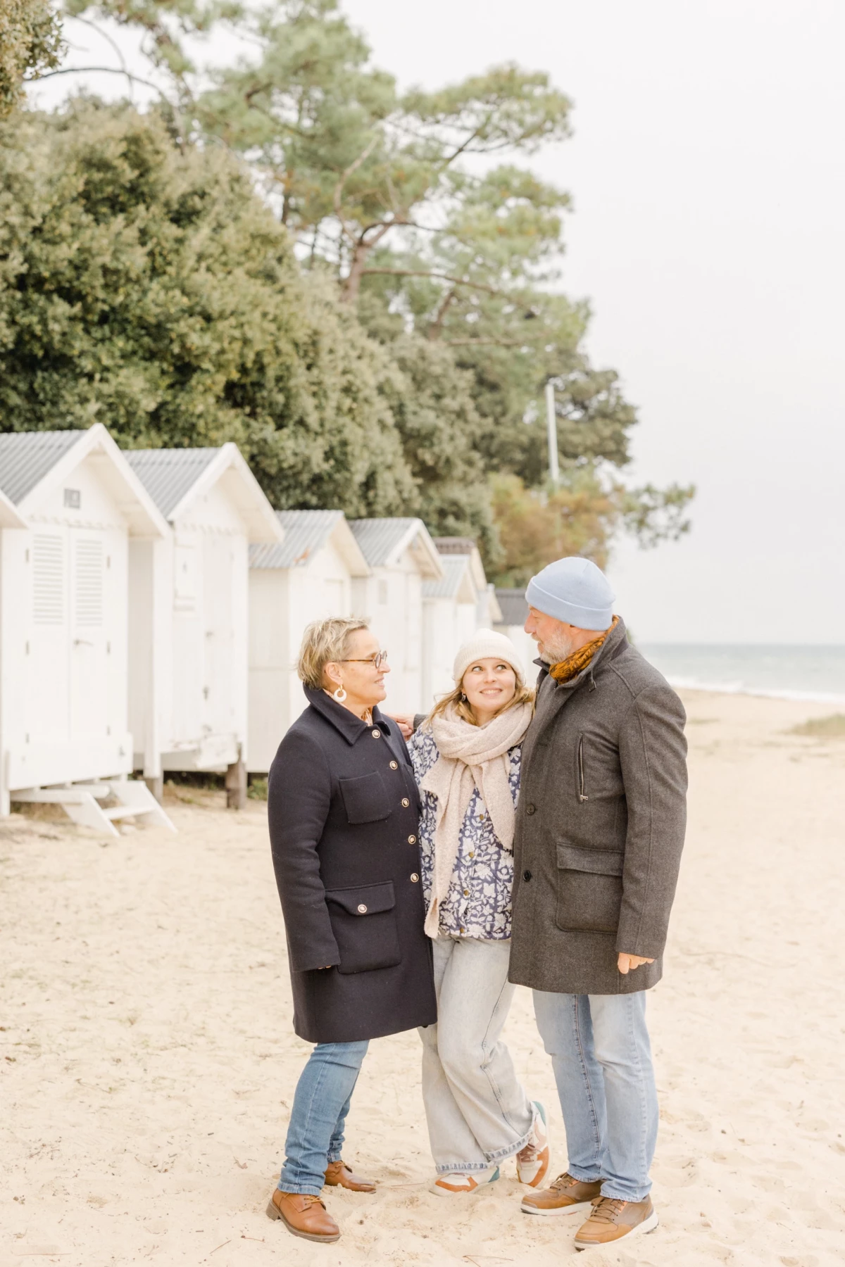 Portrait de famille multigénérationnel sur une plage avec cabanes blanches en arrière-plan