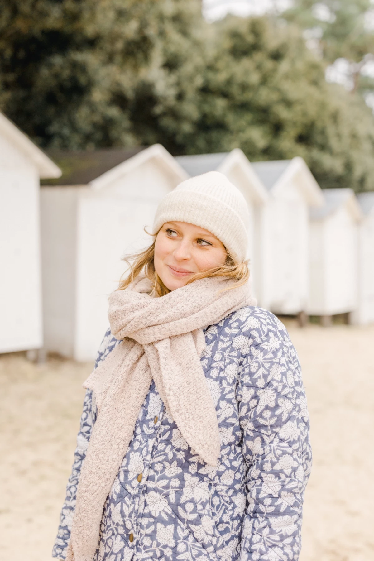 Petite fille souriante en bonnet blanc et écharpe beige sur une plage en hiver