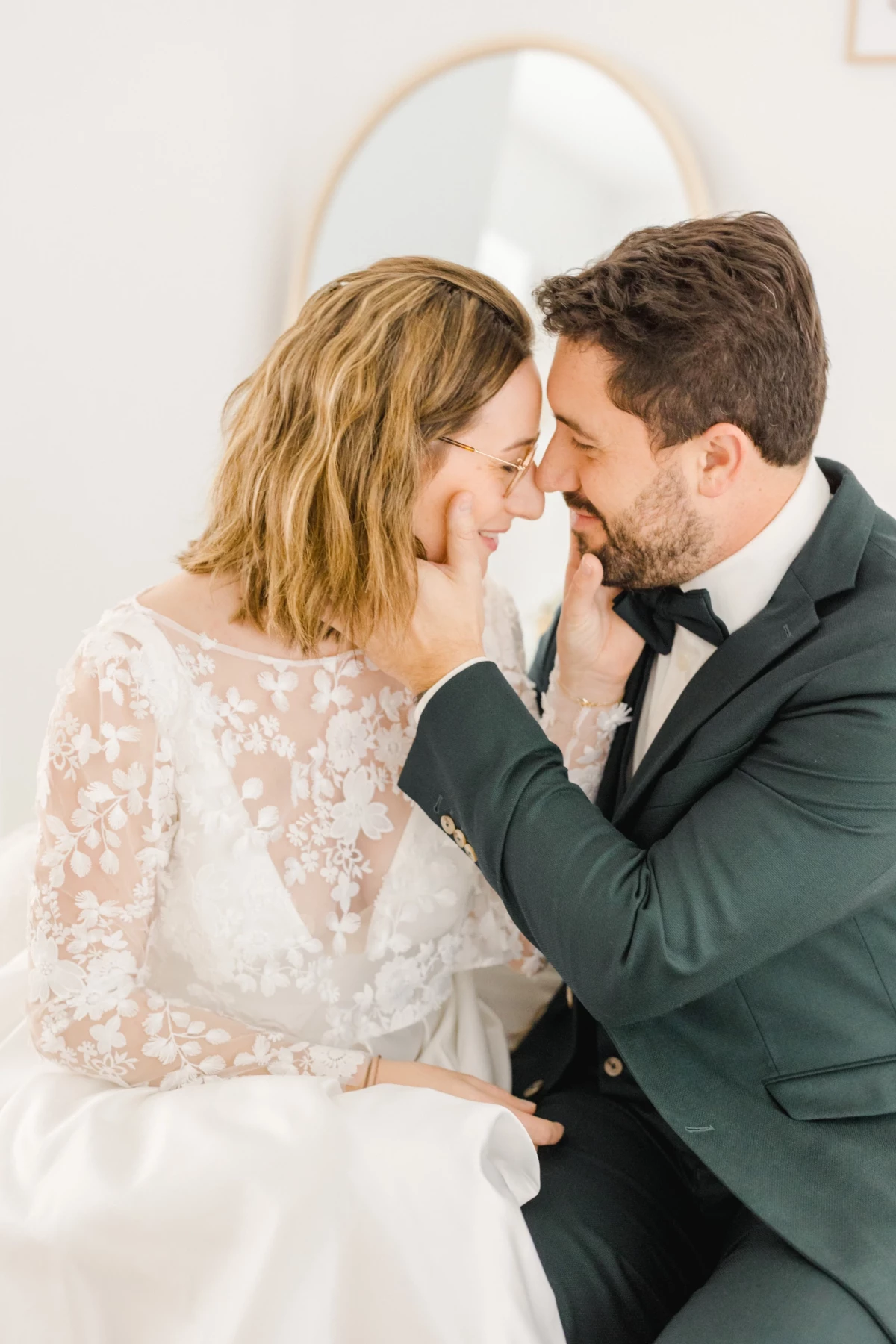Couple de mariés échangeant un regard complice en studio, robe en dentelle blanche et costume vert sapin