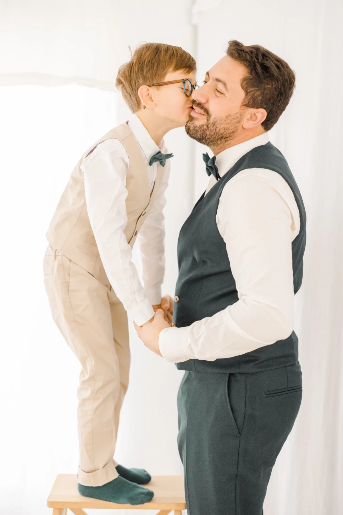 Père embrassant tendrement son jeune fils sur un tabouret en studio fond blanc