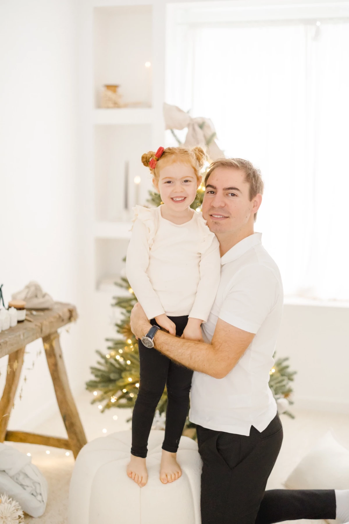 Père et fille complices dans un décor de Noël blanc et lumineux avec sapin illuminé
