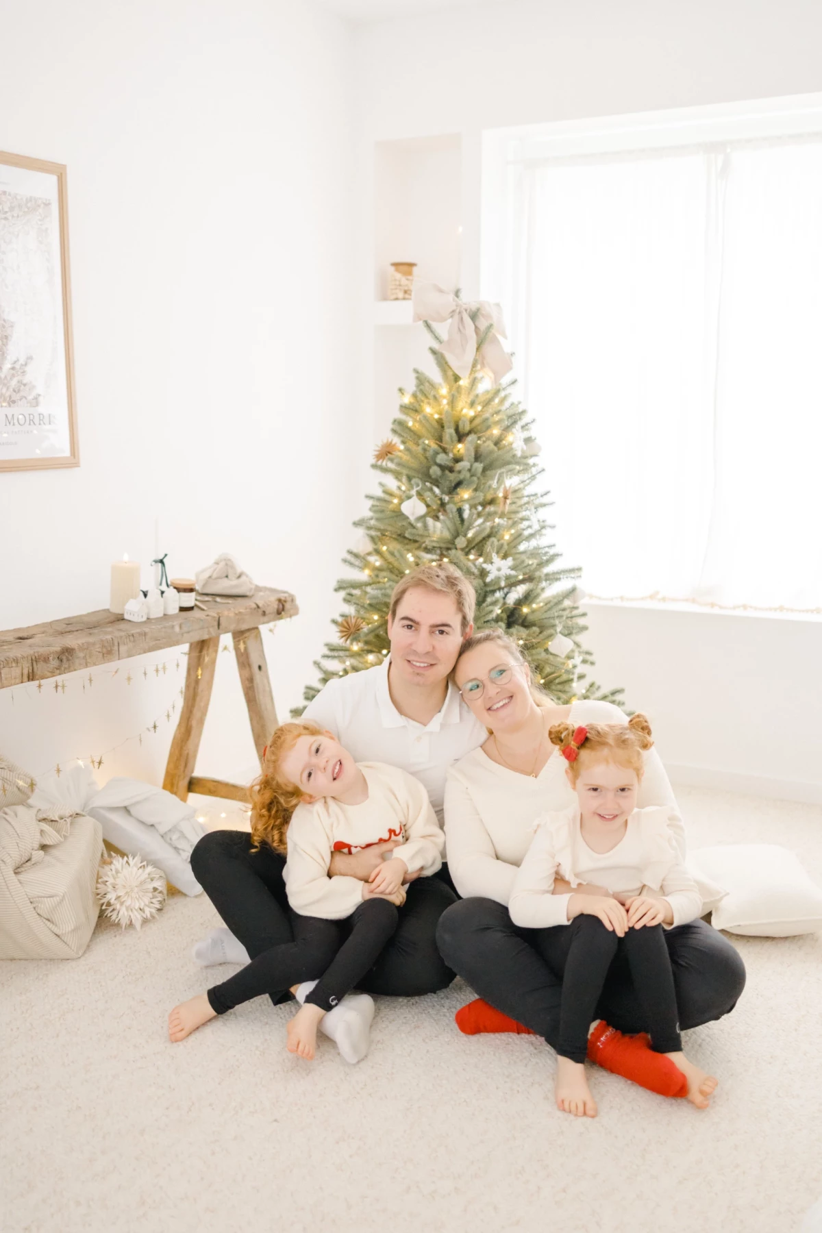 Famille souriante posant devant un sapin de Noël en studio lumineux avec décoration minimaliste