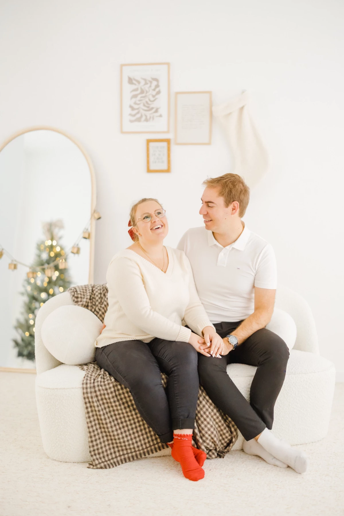 Couple complice assis sur un fauteuil blanc dans un décor de Noël minimaliste et lumineux