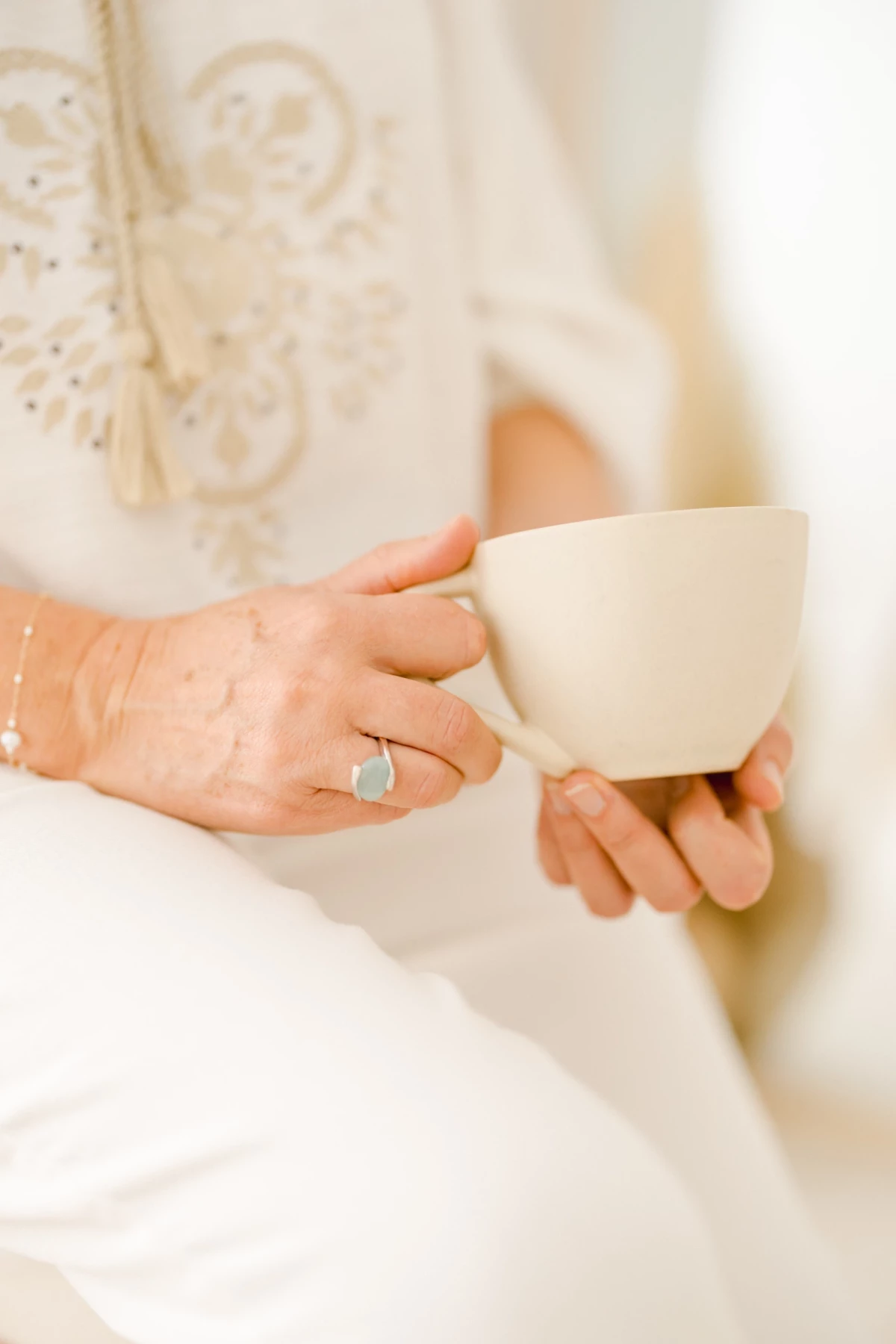 Mariée en robe blanche tenant une tasse de thé, bague visible sur sa main lors des préparatifs