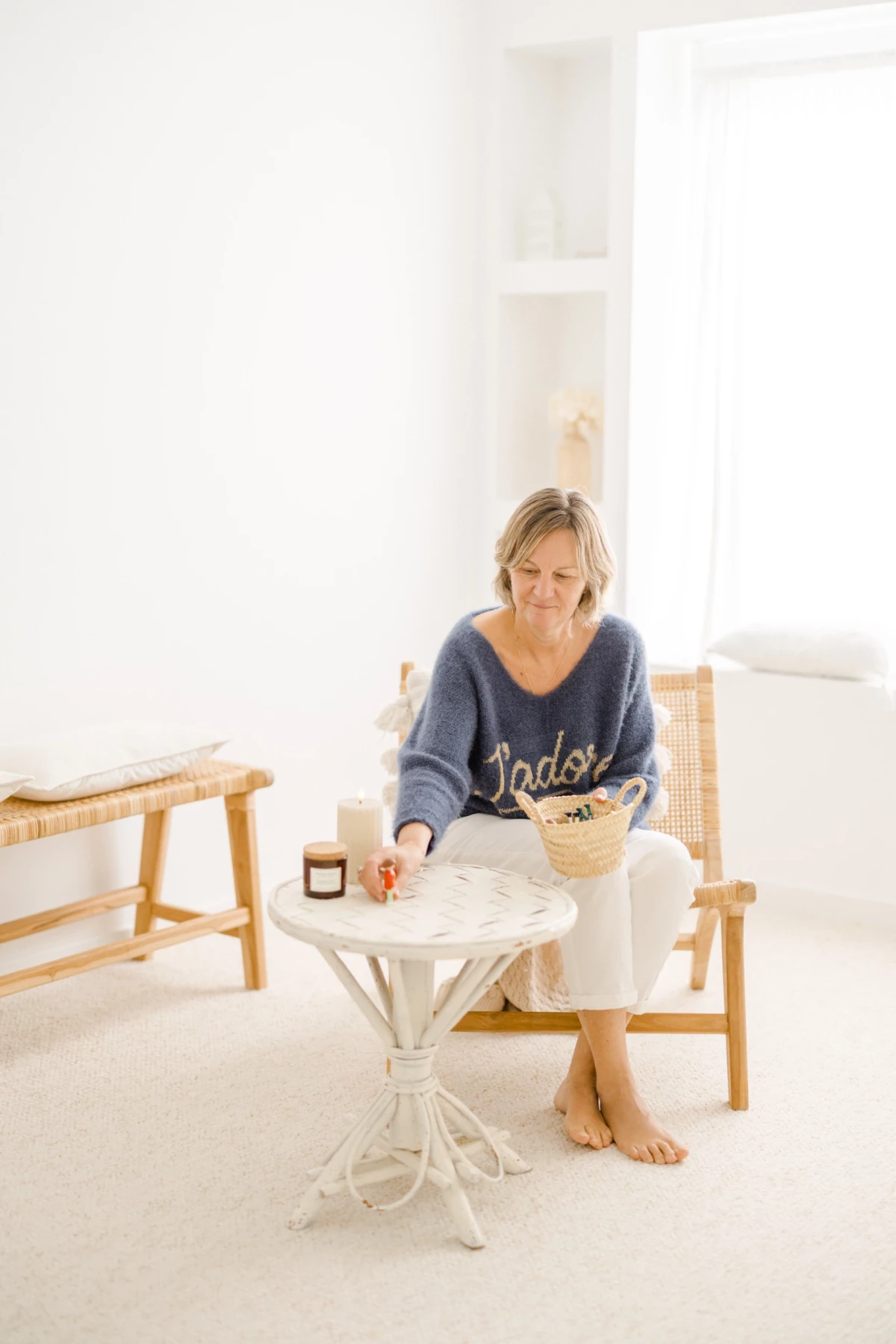 Femme en pull gris assise dans un fauteuil en rotin, savourant un moment de détente avec une bougie