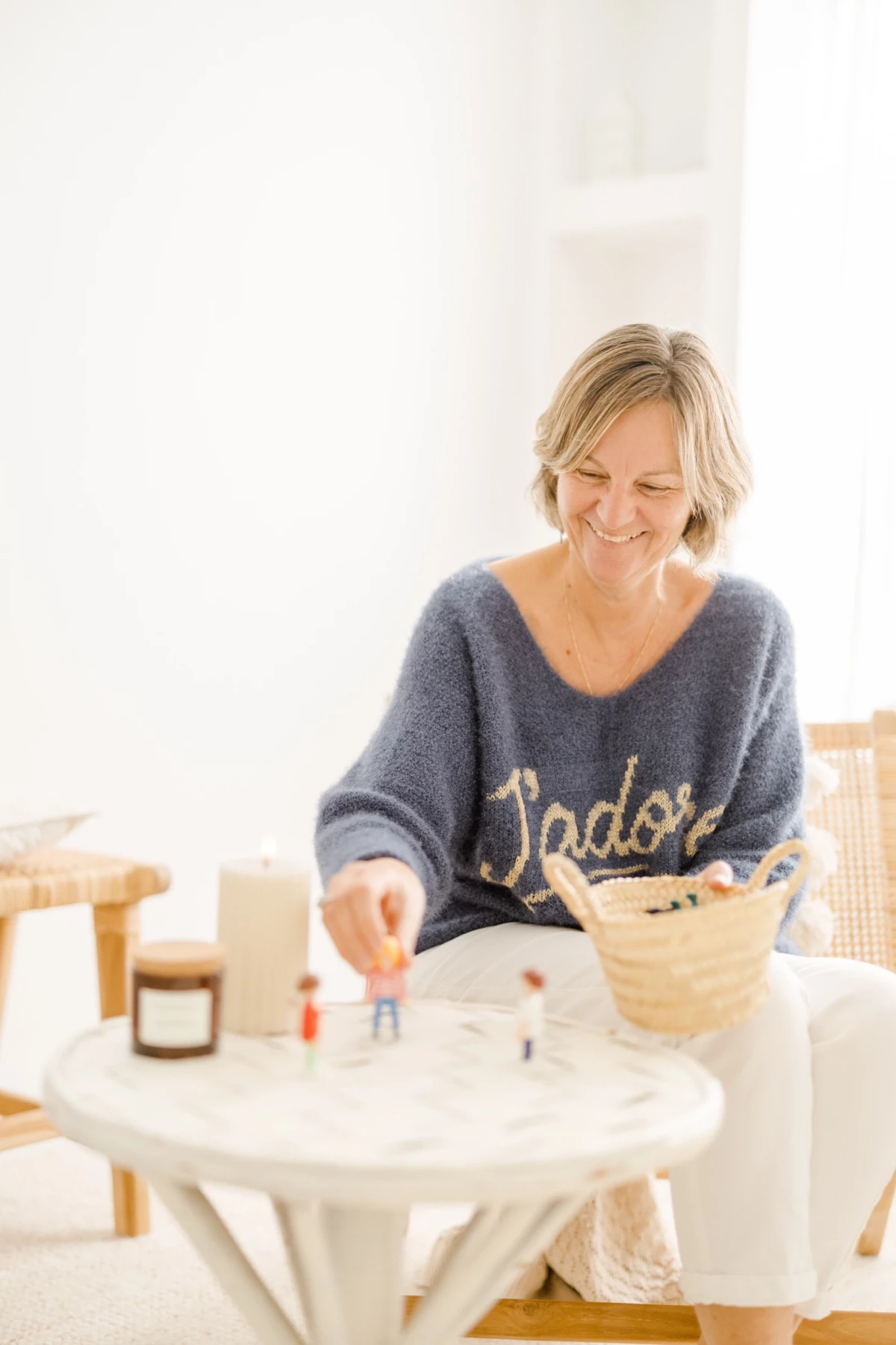 Femme blonde souriante créant un objet artisanal sur une table blanche dans un intérieur lumineux
