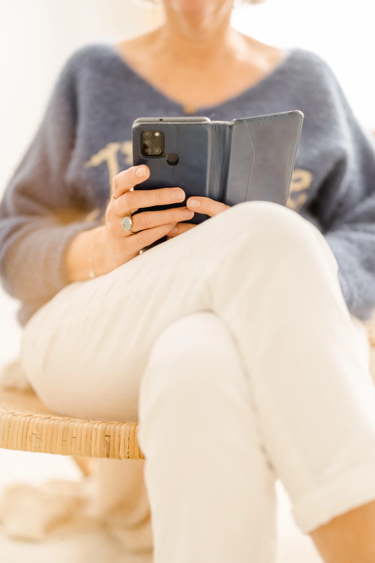 Future maman tenant son téléphone, vêtue d'un pull gris confortable et d'un pantalon blanc écru