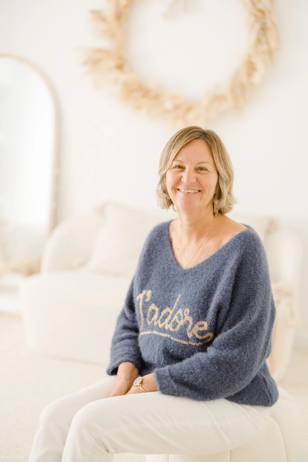 Portrait professionnel d'une femme souriante assise sur un fauteuil blanc en pull bleu décontracté