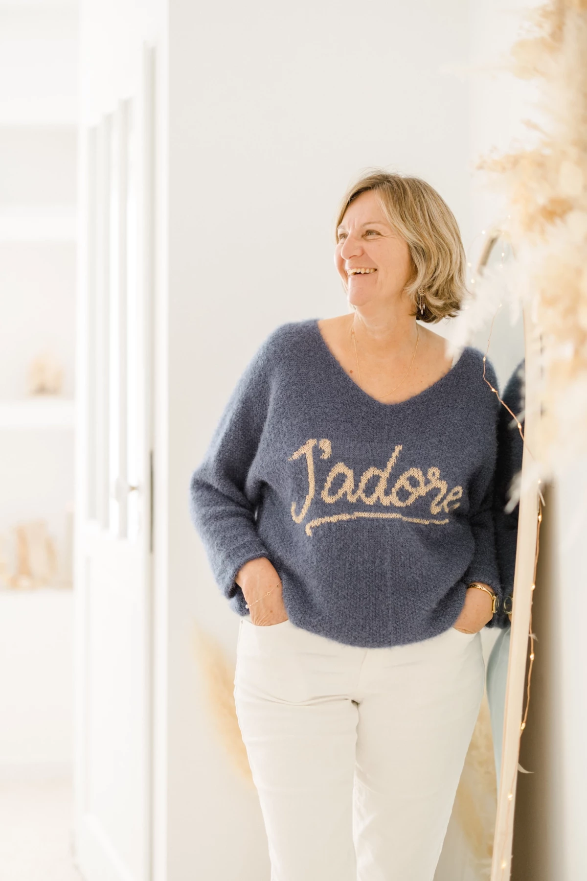 Femme souriante en pull bleu marine brodé J'adore et pantalon blanc, portrait corporate lumineux