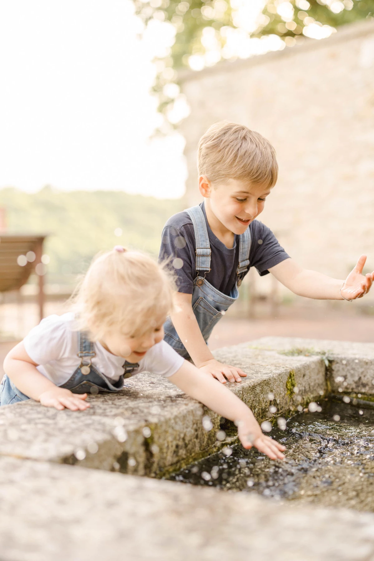 Deux enfants jouant ensemble près d'une fontaine en pierre, explorant l'eau avec émerveillement