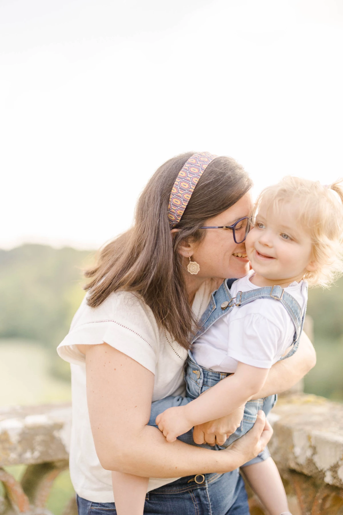 Mère embrassant tendrement son enfant en salopette dans la lumière dorée d'un paysage champêtre