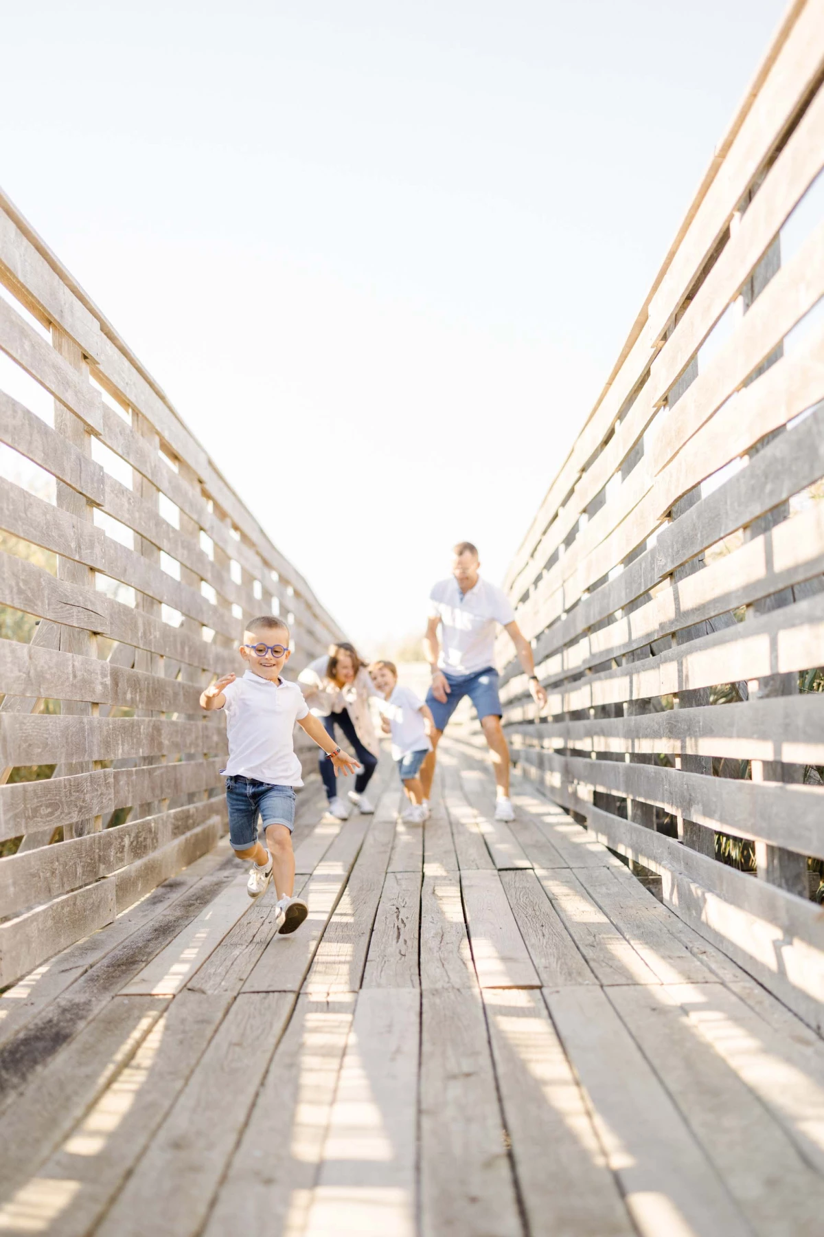 Famille joyeuse courant sur un ponton en bois, enfant devant, parents et fratrie suivant en riant