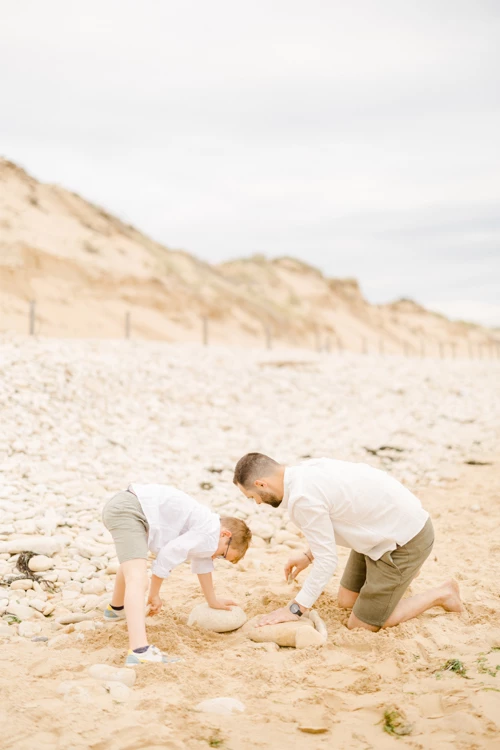 Père et fils jouant ensemble dans le sable d'une plage déserte, vêtus de blanc