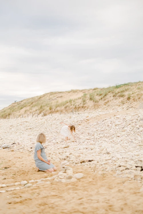 Mère et enfant jouant sur une plage de sable avec dunes herbeuses sous un ciel nuageux
