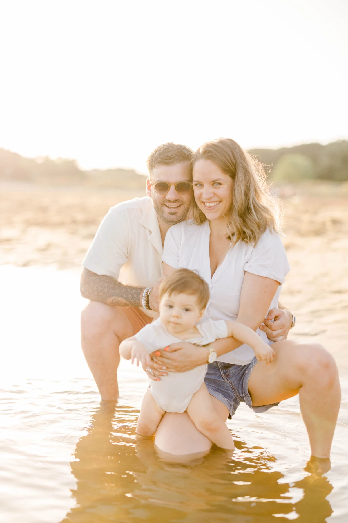 Famille complice posant dans l'eau à la plage au coucher du soleil avec leur enfant