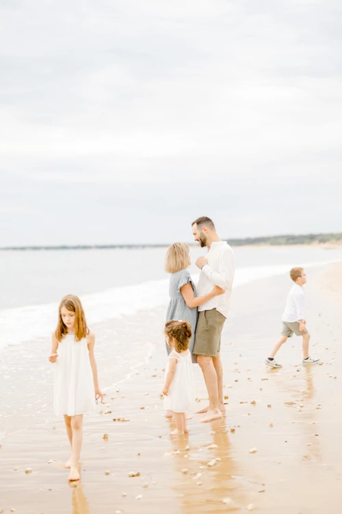 Famille complice se promenant pieds nus sur une plage de sable fin sous un ciel nuageux