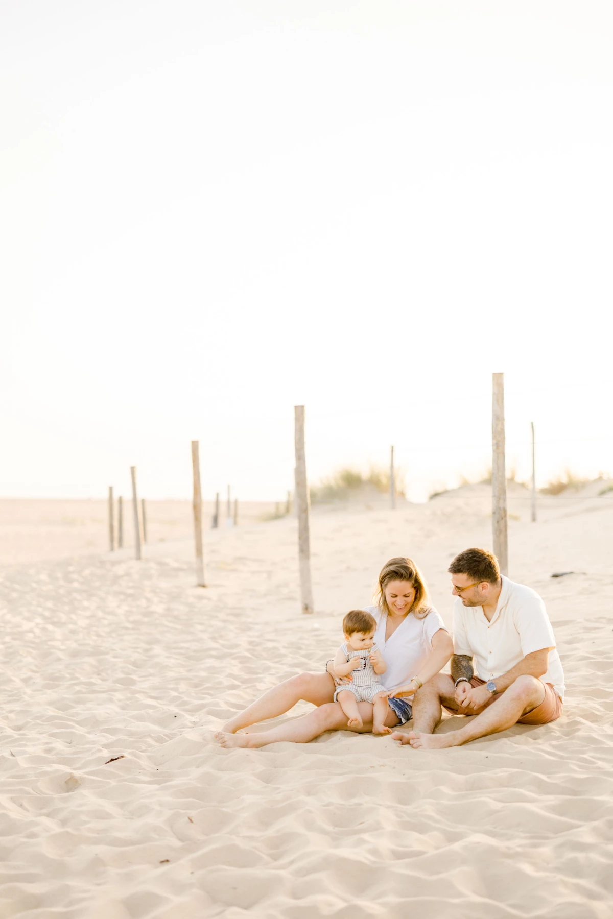 Famille de quatre personnes assise sur le sable d'une plage au coucher du soleil, moments de tendresse