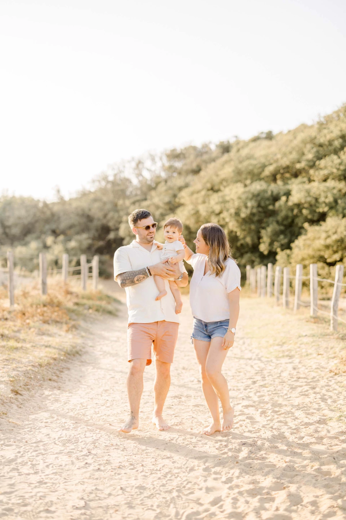 Famille de trois personnes sur un chemin de sable, parents et leur enfant dans une lumière dorée