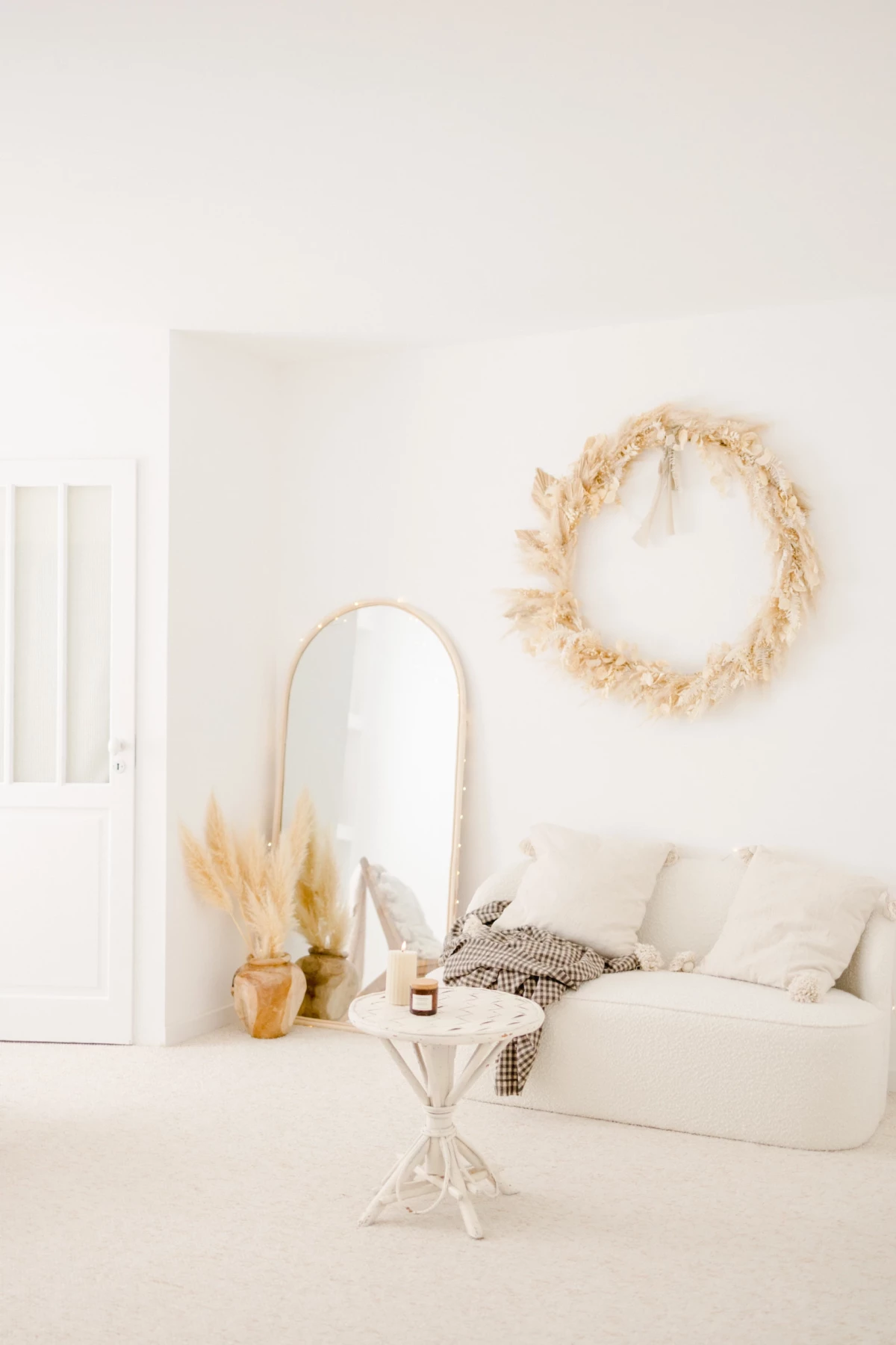 Salon minimaliste blanc et beige avec canapé, miroir arche et couronne de fleurs séchées