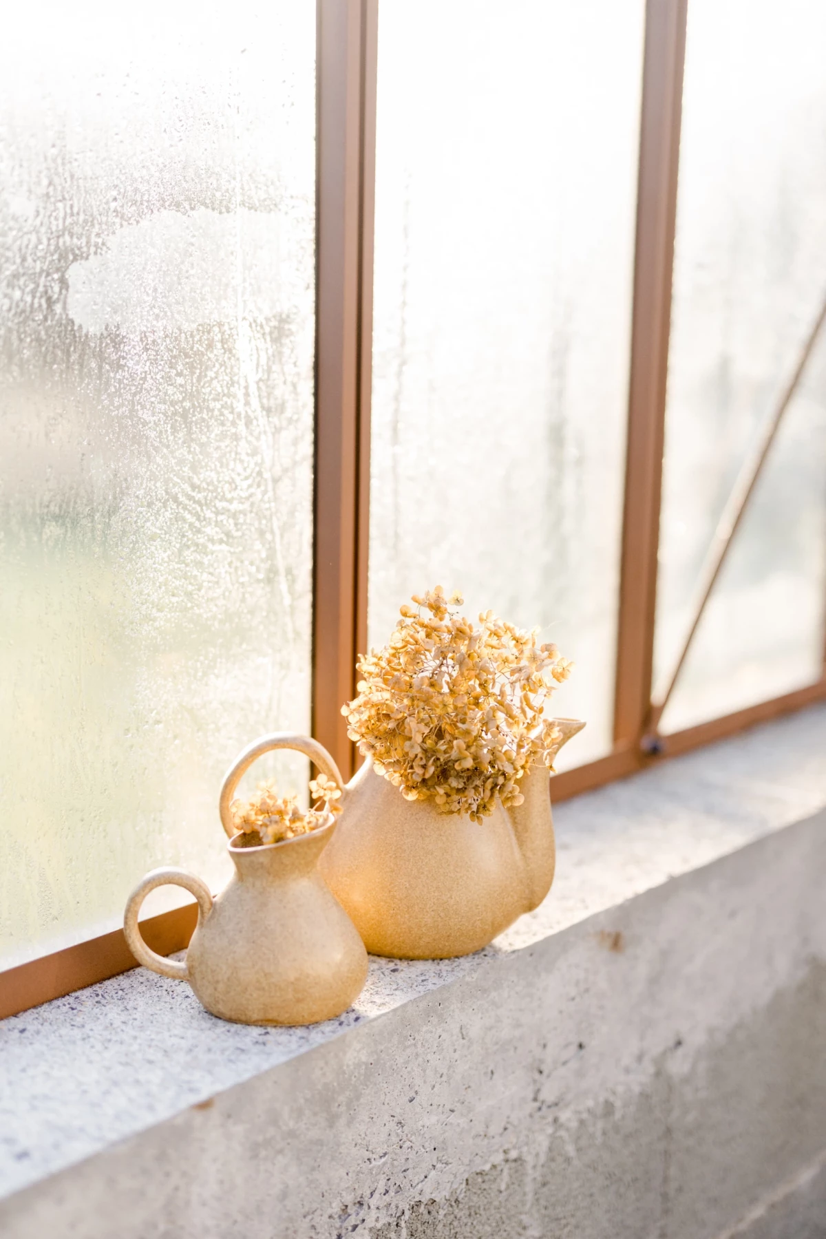 Vases en céramique beige avec fleurs séchées dorées posés sur rebord de fenêtre en bois naturel