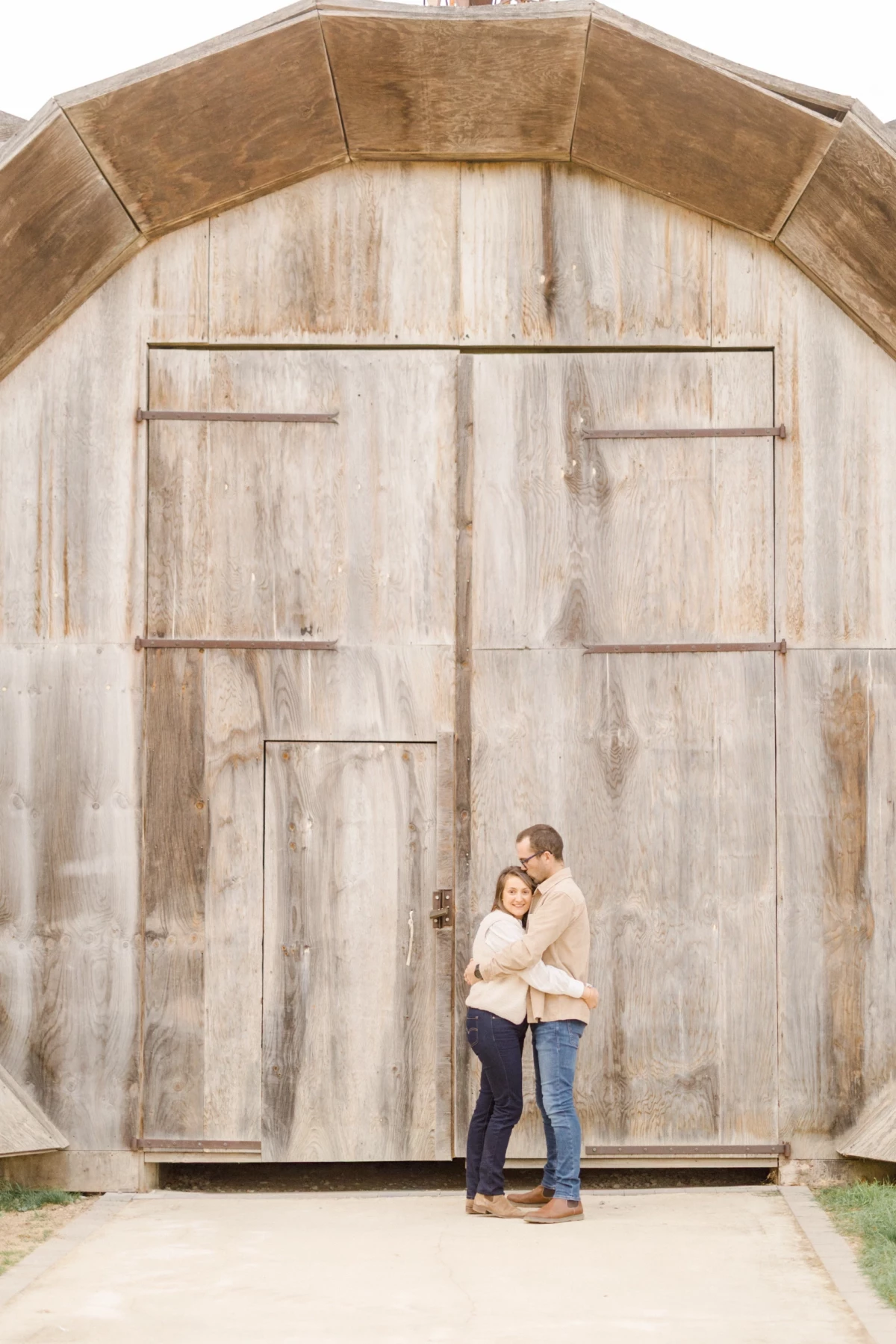 Couple enlacé devant une porte de grange rustique lors d'une séance grossesse en extérieur
