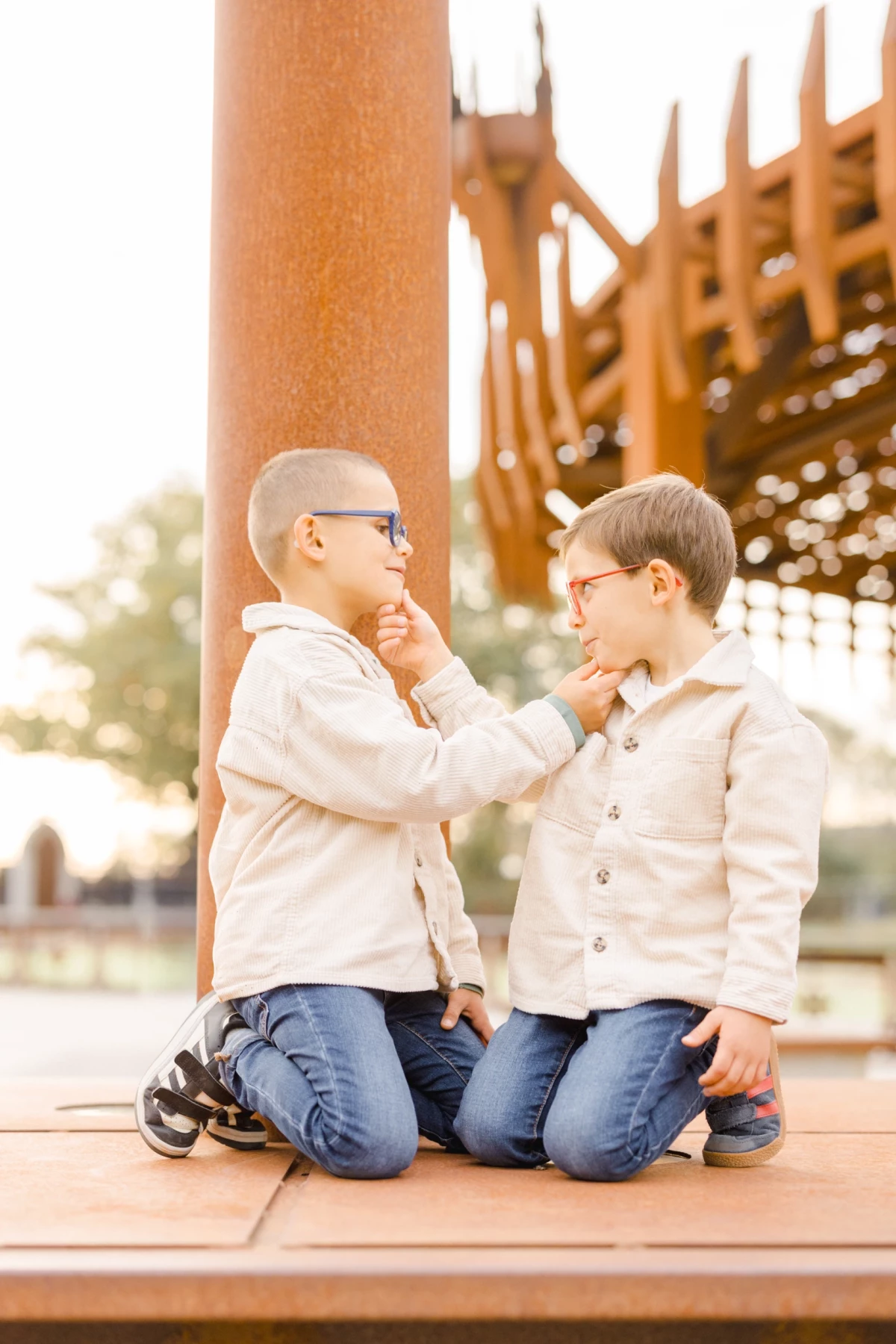 Deux jeunes frères complices se regardent en souriant, assis sur une structure en bois au parc