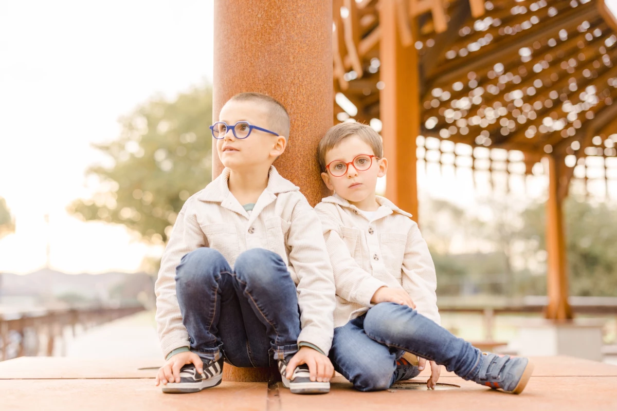 Deux jeunes frères assis côte à côte sous une pergola en bois, regard complice et tenue assortie