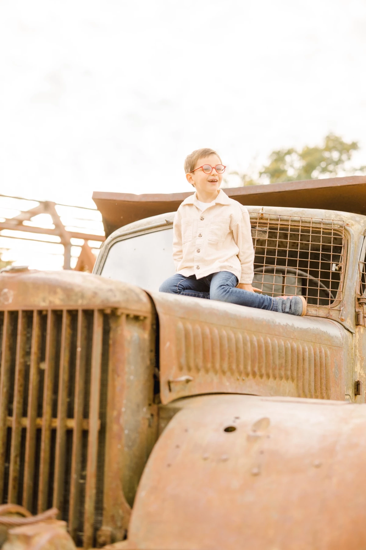Jeune garçon assis sur un vieux camion rouillé dans un champ baigné de lumière dorée