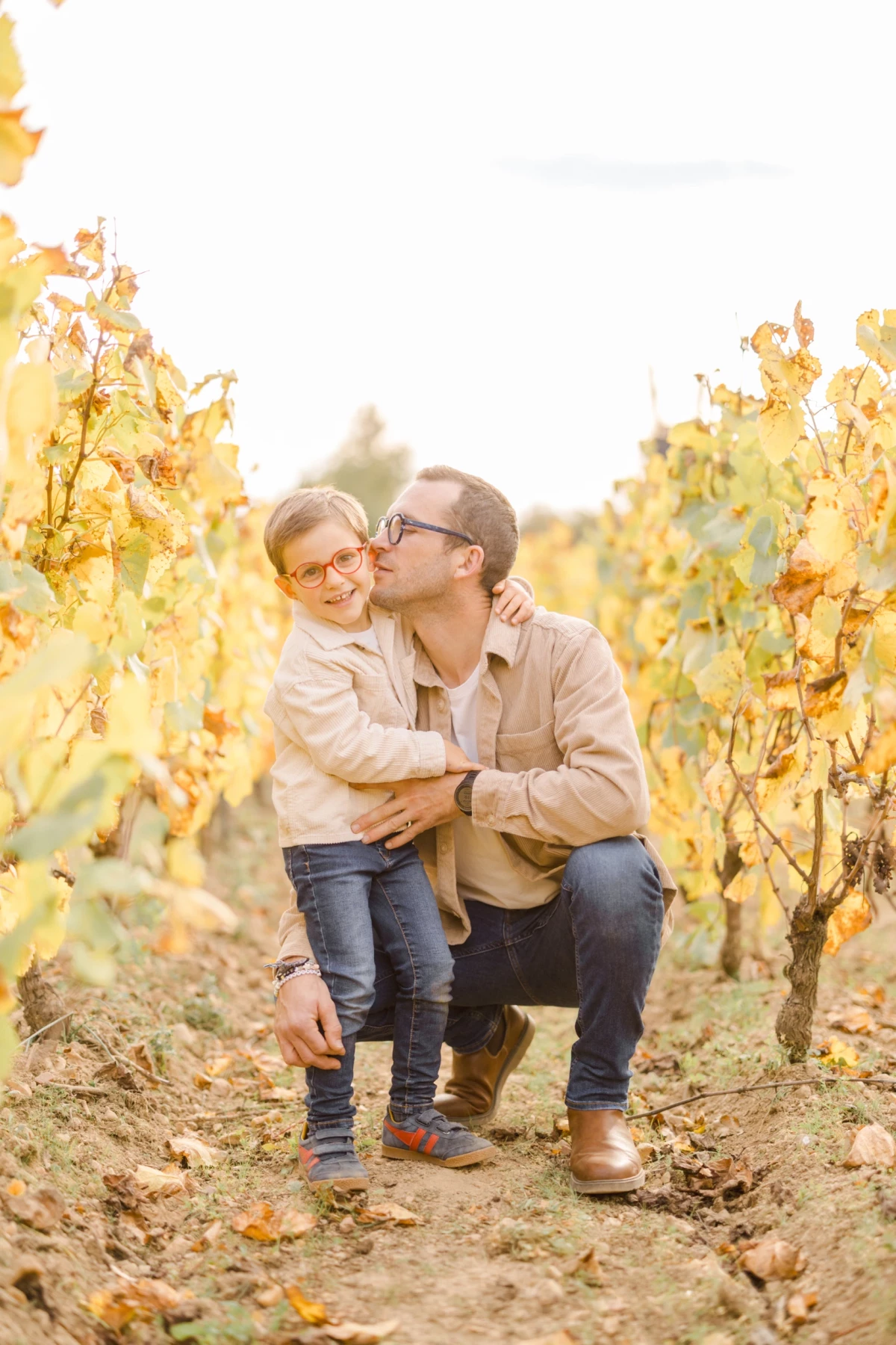 Père embrassant tendrement son enfant dans un vignoble aux couleurs automnales dorées