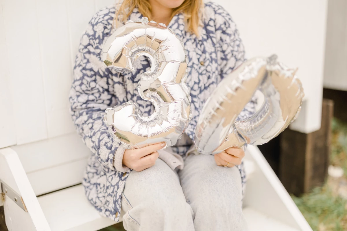 Enfant en pyjama douillet tenant des ballons argentés chiffre 3 pour célébrer son anniversaire à Noël