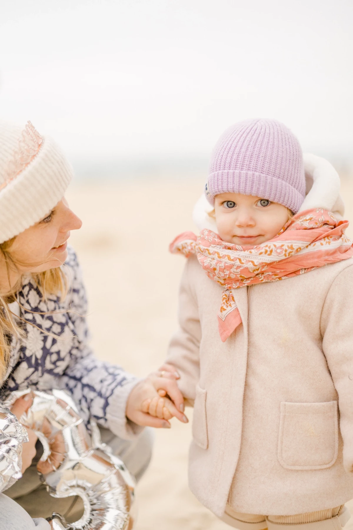 Deux fillettes complices sur une plage en tenue d'hiver, échangeant un regard tendre