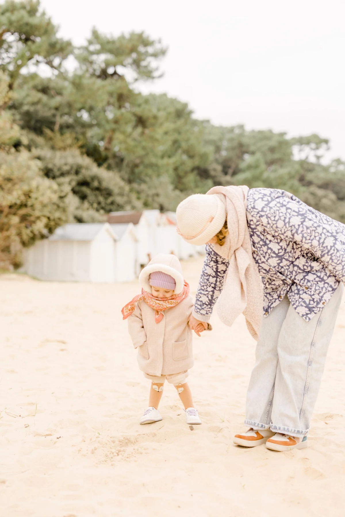 Mère aidant son enfant à marcher sur une plage de sable fin, moment de tendresse et d'apprentissage