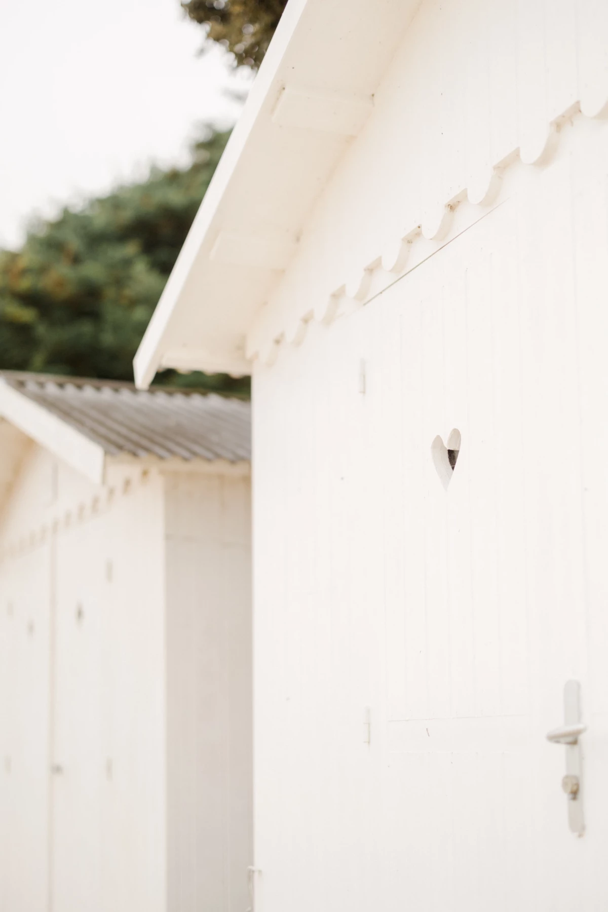 Détail architectural d'une bâtisse blanche épurée avec porte et lampe murale dans une lumière naturelle douce