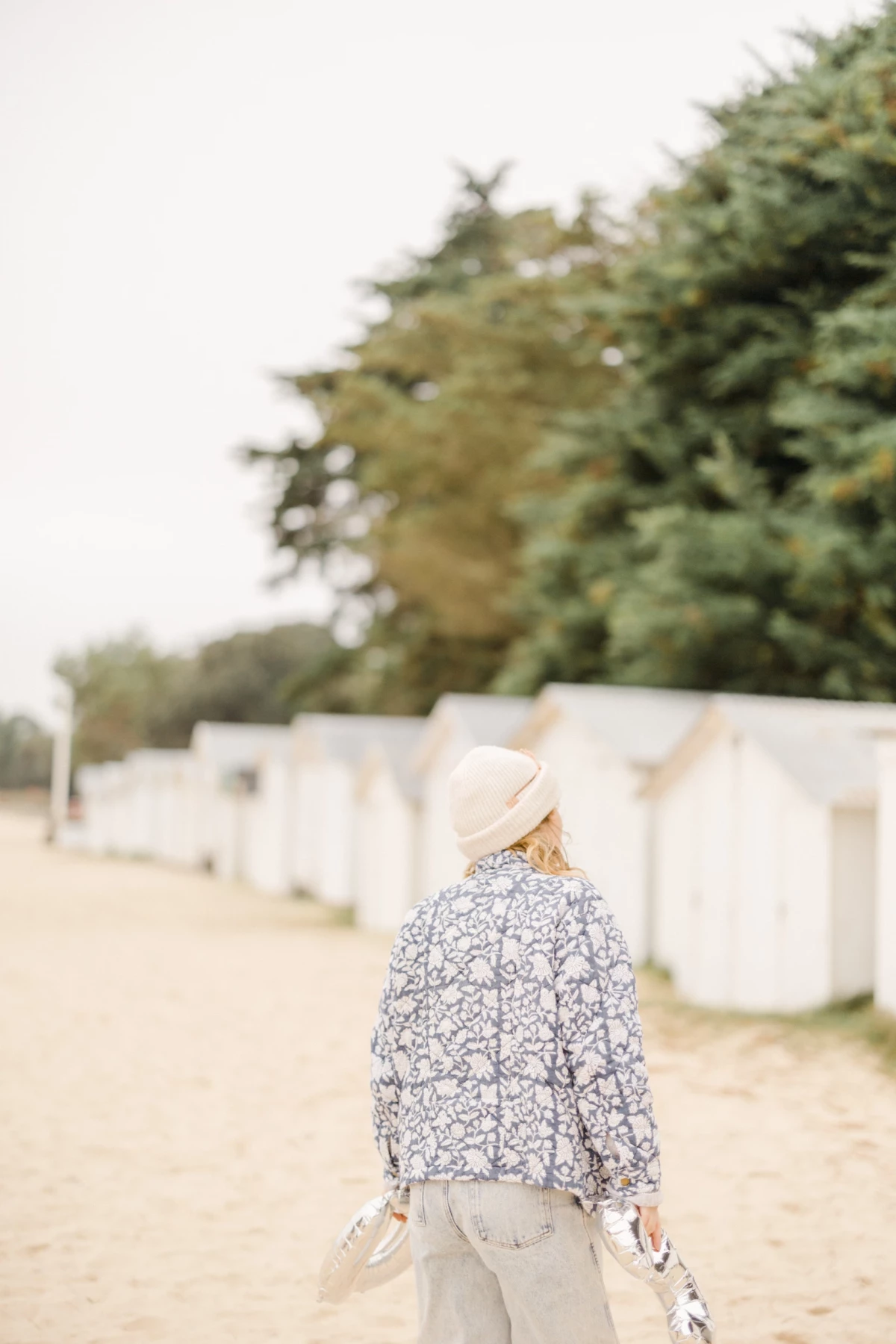 Mariée de dos en chemise fleurie et chapeau beige marchant dans une allée bordée d'arbres et de murets blancs