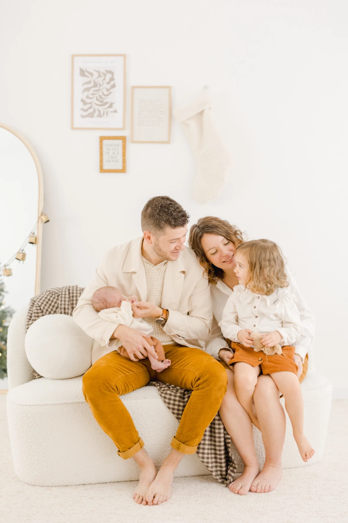 Jeune famille posant sur un canapé blanc avec leur nouveau-né et leur fille, ambiance douce et lumineuse