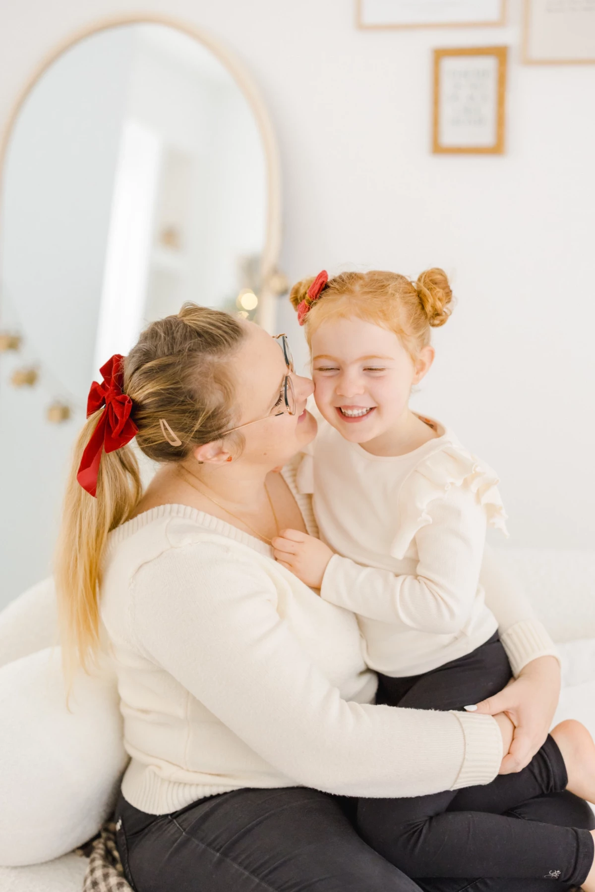 Mère et fille complices partageant un moment de tendresse, habillées en blanc avec nœuds rouges assortis