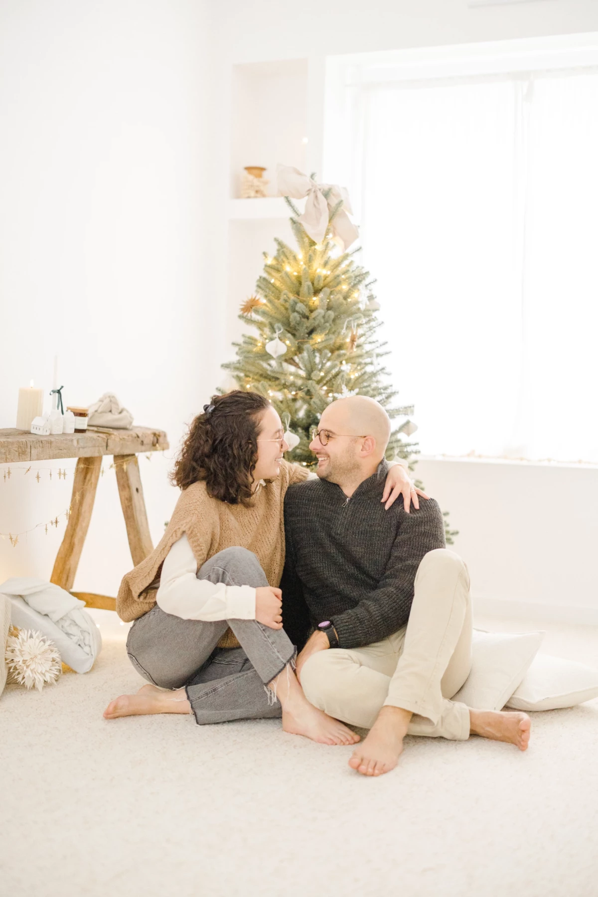 Couple enlacé devant un sapin de Noël doré dans un décor studio minimaliste blanc