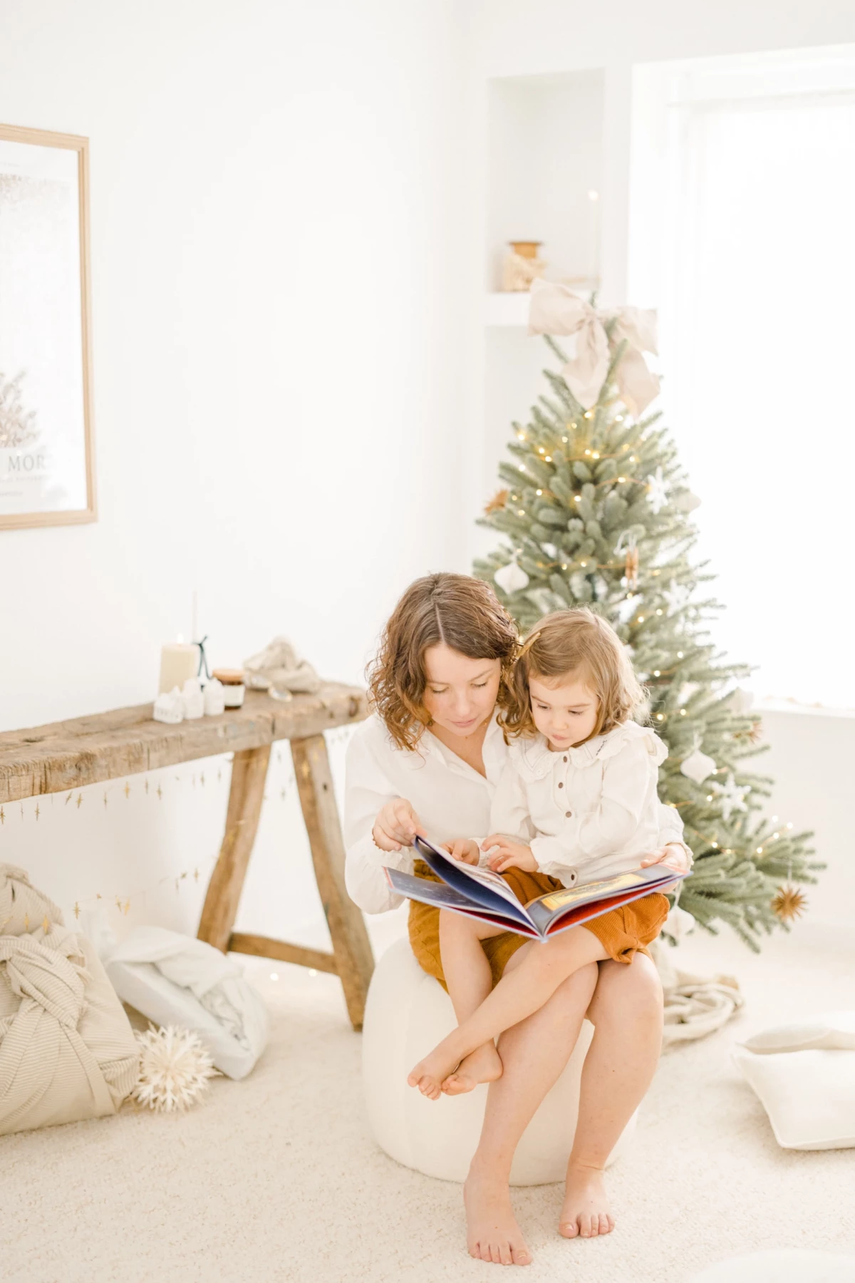 Mère et fille lisant ensemble près d'un sapin de Noël dans un intérieur blanc lumineux