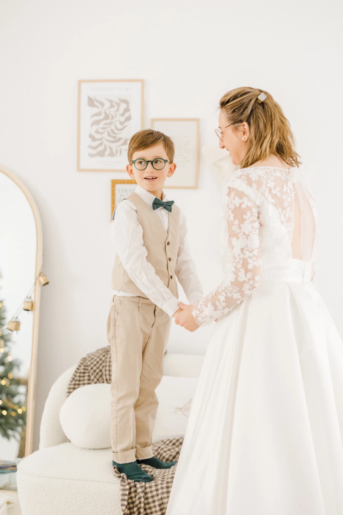 Mariée en robe de dentelle blanche tenant la main de son petit garçon en costume beige et nœud papillon vert