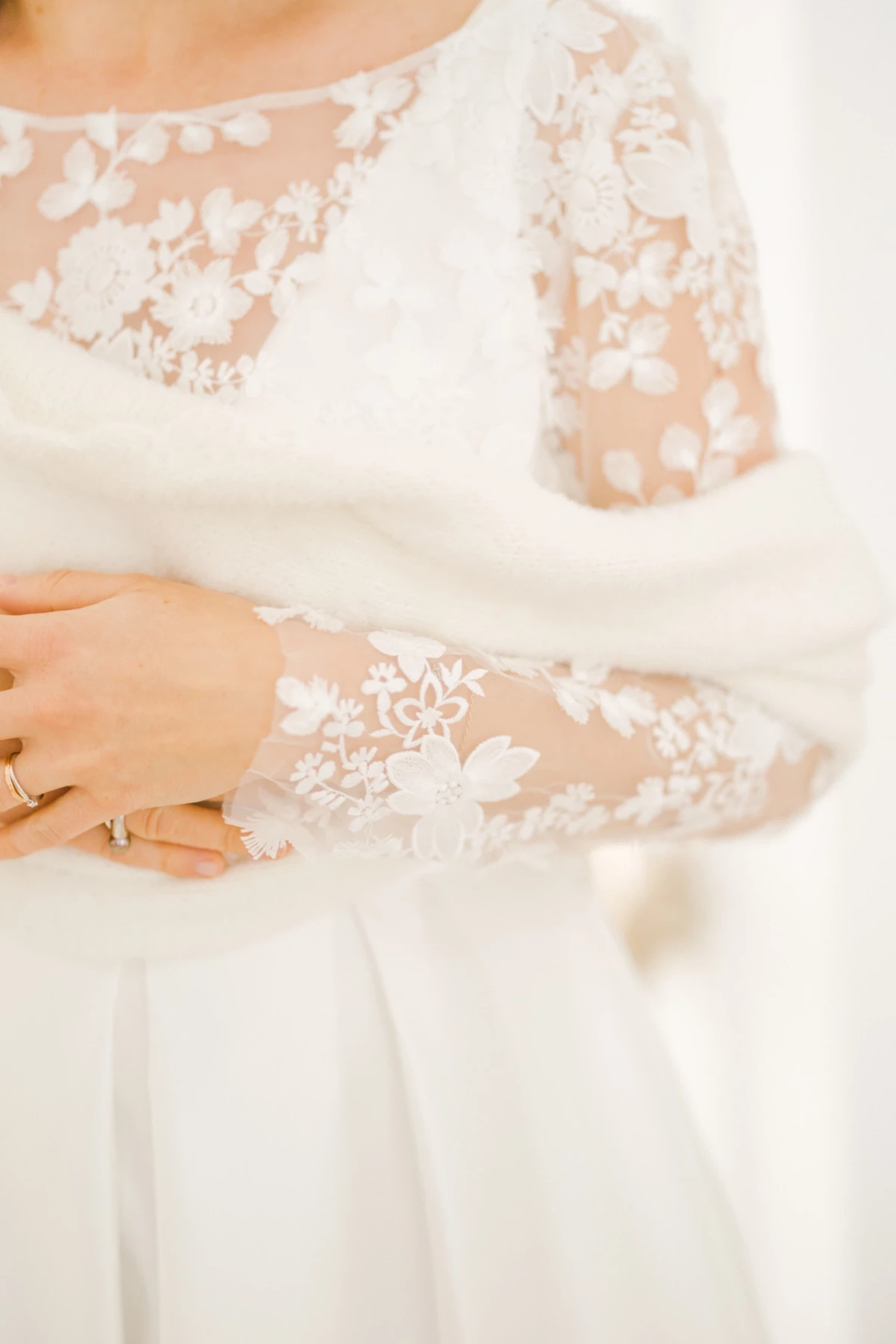 Détail des manches en dentelle blanche d'une robe de mariée avec broderies florales et main ornée de bagues