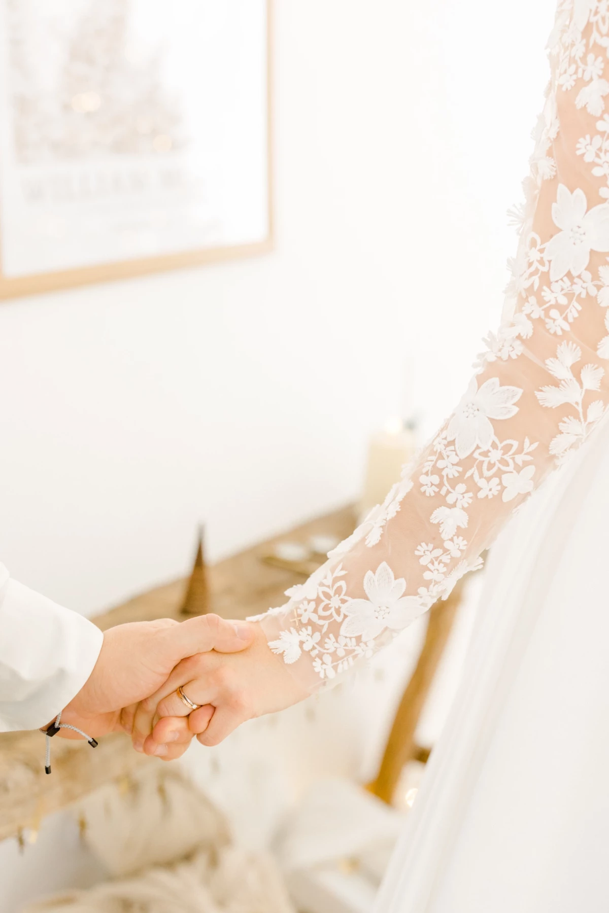 Main de mariée portant une alliance sur sa robe en dentelle blanche ornée de motifs floraux délicats